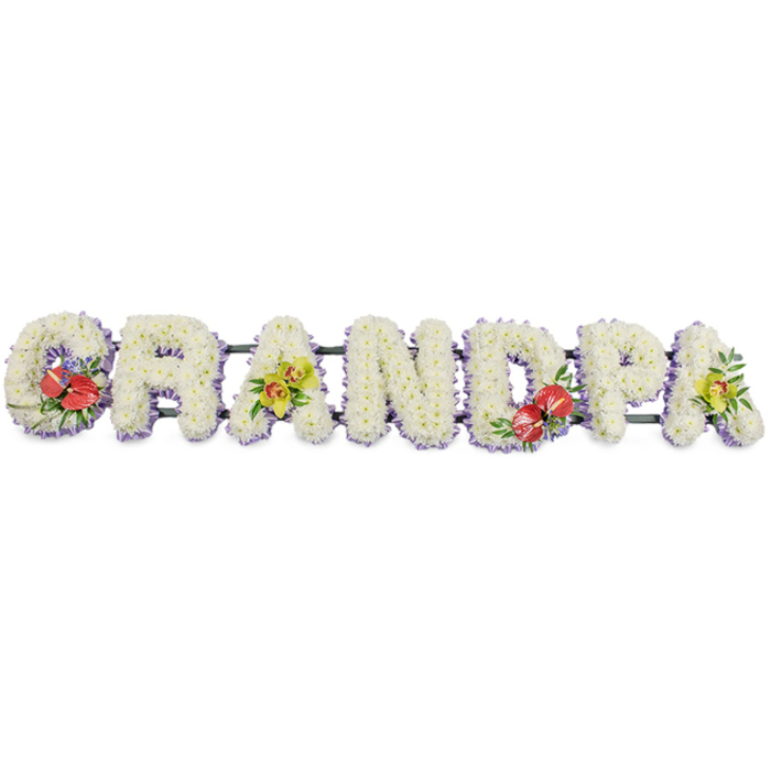 In this image, a beautifully composed funeral tribute spells out the word "GRANDPA" in large, block capital letters, laid out in a straight horizontal line against a bright white background that highlights every nuance of the design. Each letter is made up entirely of small, white chrysanthemums, expertly arranged so that their soft petals create a thick, even cushion of texture with no visible gaps, radiating a feeling of calm, purity, and respectful remembrance. At the base of every letter runs a fine band of pale lavender ribbon, a cool, understated edge that defines the shapes and gently lifts the white flowers from the supporting structure beneath. The letters sit on a dark green frame, discreetly tucked away behind the blooms, giving the tribute the strength to be moved and displayed as one connected piece. To break the simplicity of the white and add emotional emphasis, the florist has woven in vibrant accent sprays. On the "G" and the "D," clusters of deep red anthuriums, with their waxy, heart-shaped petals and upright yellow spadices, nestle into rich, dark green foliage, punctuated by tiny purple flowers that add a hint of depth and contrast. On the first "A" and the last "A," clusters of yellow-green orchids, likely cymbidiums, arch gracefully over the chrysanthemums, their delicate petals and speckled throats lending a touch of refined beauty. Glossy green leaves frame the orchids, softening the edges of the letters. The overall effect is both traditional and contemporary, the kind of bespoke "Grandpa" floral lettering that families in Peckham might choose to honour a beloved grandfather at a funeral service or graveside committal, reflecting both love and the character of the person being remembered.