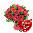 The photograph features a richly coloured, romantic gift arrangement that combines classic red roses with a bold heart balloon, captured against a bright white backdrop reminiscent of minimalist interiors in modern Peckham homes. At the centre is a dense cluster of deep crimson roses, approximately one to two dozen blooms forming a compact, rounded bouquet. The petals have a distinctly velvety appearance, and the roses show different stages of opening: some are wide and full, revealing intricate swirls of layered petals, while others are more tightly formed, giving the composition a sense of natural progression and life. Interlaced among the roses is an abundance of dark green foliage, its glossy leaves providing structure and a cool counterbalance to the vivid red. These stems are arranged in a stylish ruby-red glass vase, whose clear body and fluted sides create subtle vertical patterns of light and shadow, hinting at careful craftsmanship similar to pieces found in independent Peckham boutiques. In the lower right area of the image, partially overlapping the bouquet and vase, a shiny red heart-shaped foil balloon leans forward. It has a smooth, reflective surface that picks up highlights, and across the balloon, elegant white cursive script clearly spells out the words "I Love You." A silver-toned Cupid-style arrow is illustrated as piercing diagonally through the heart, reinforcing the unmistakably romantic theme. The pure white background strips away distractions, allowing the rich reds of the roses and balloon, the cool silver of the arrow, and the fresh greens of the foliage to stand out with striking clarity. Overall, the image conveys a mood of heartfelt affection and joyous celebration, perfect for imagining a Valentine's Day surprise or anniversary delivery anywhere in Peckham.